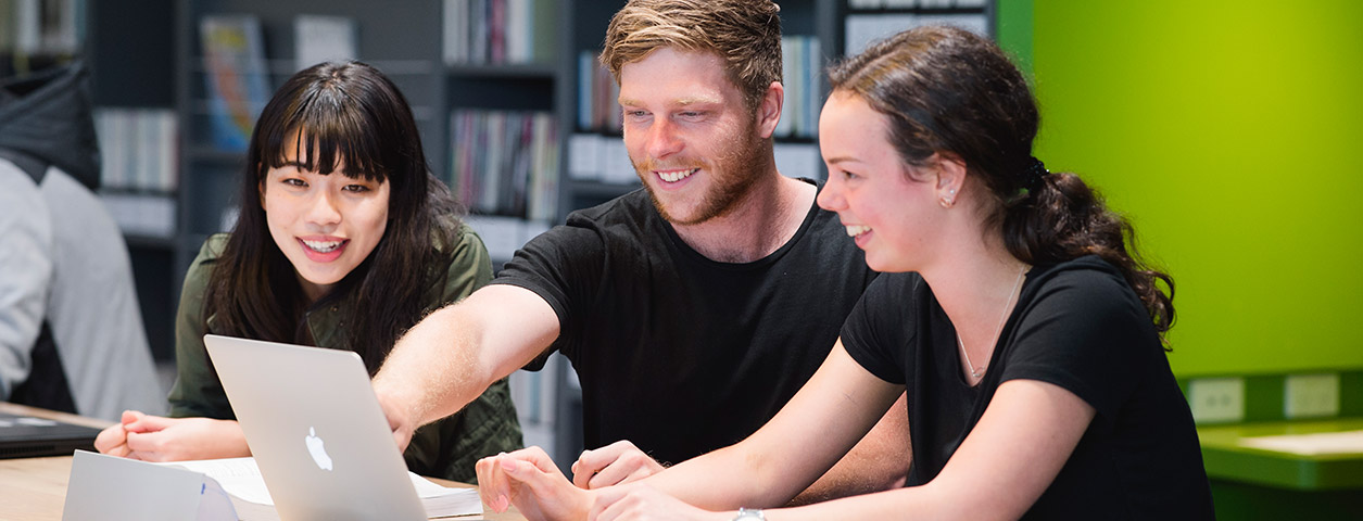 Three students work on a single laptop