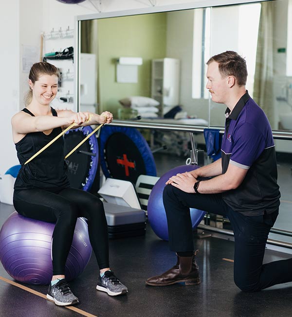 ACU Staff member assisting a woman with an exercise routine in the gym.