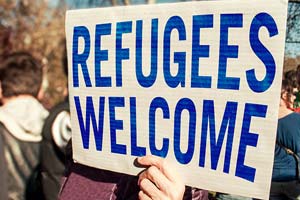 A hand holding a large sign with words the "Refugees welcome".