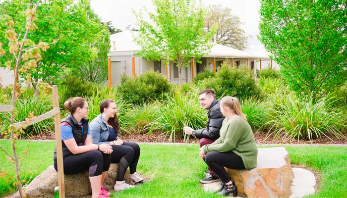 Four young students sit on a green lawn, talking