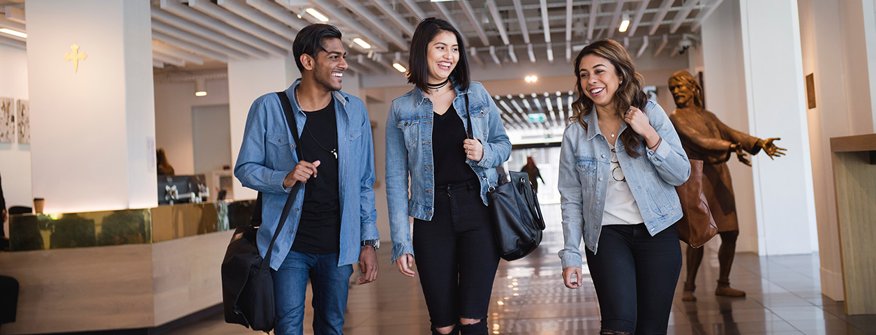 Three young students walk side by side through campus